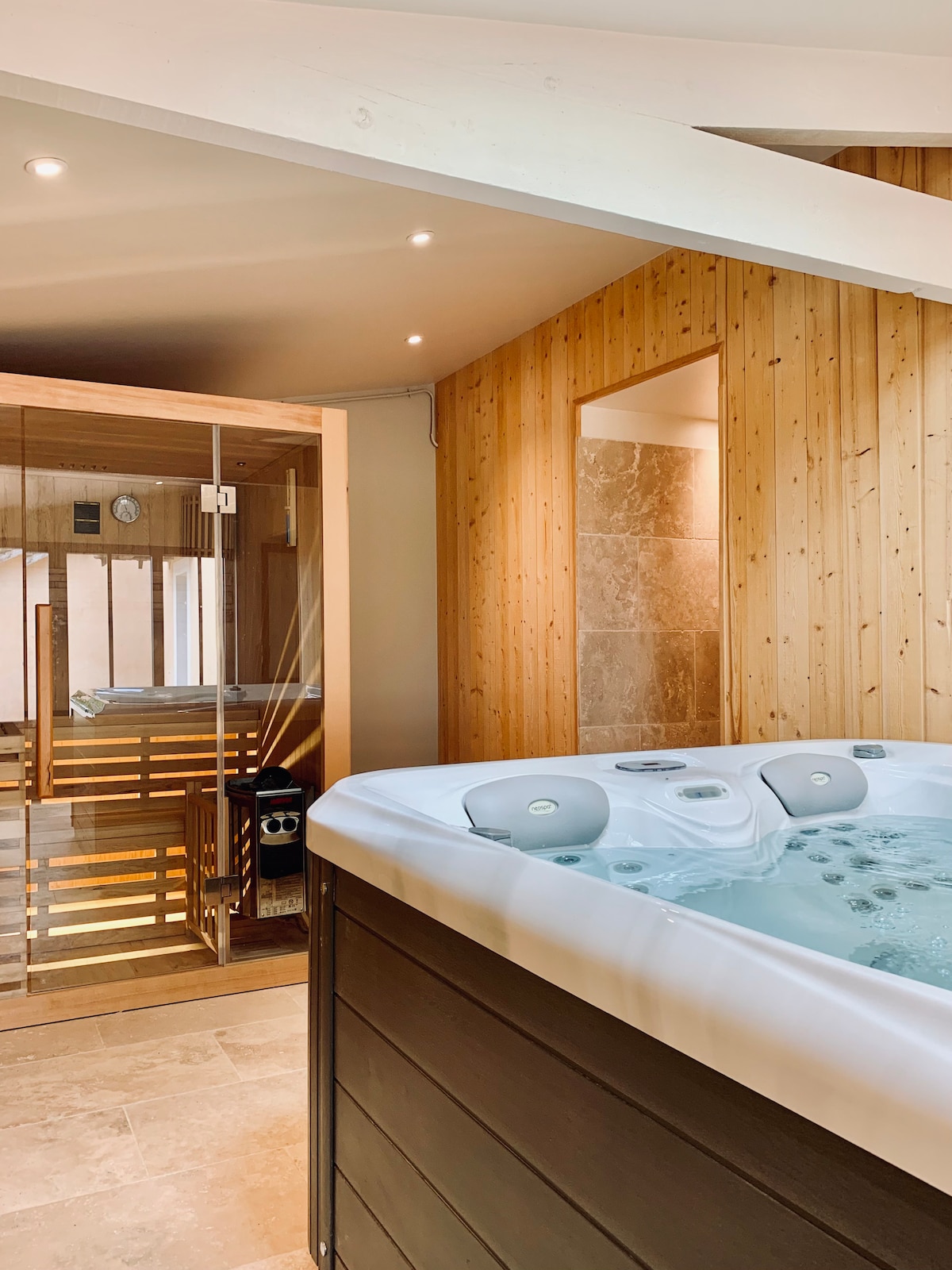 A spacious relaxation area features a well-appointed jacuzzi and a sauna, surrounded by wooden paneling. Soft lighting illuminates the space, and warm tones enhance the calming atmosphere. A glass door provides a glimpse into the sauna, ensuring privacy while promoting a peaceful retreat.