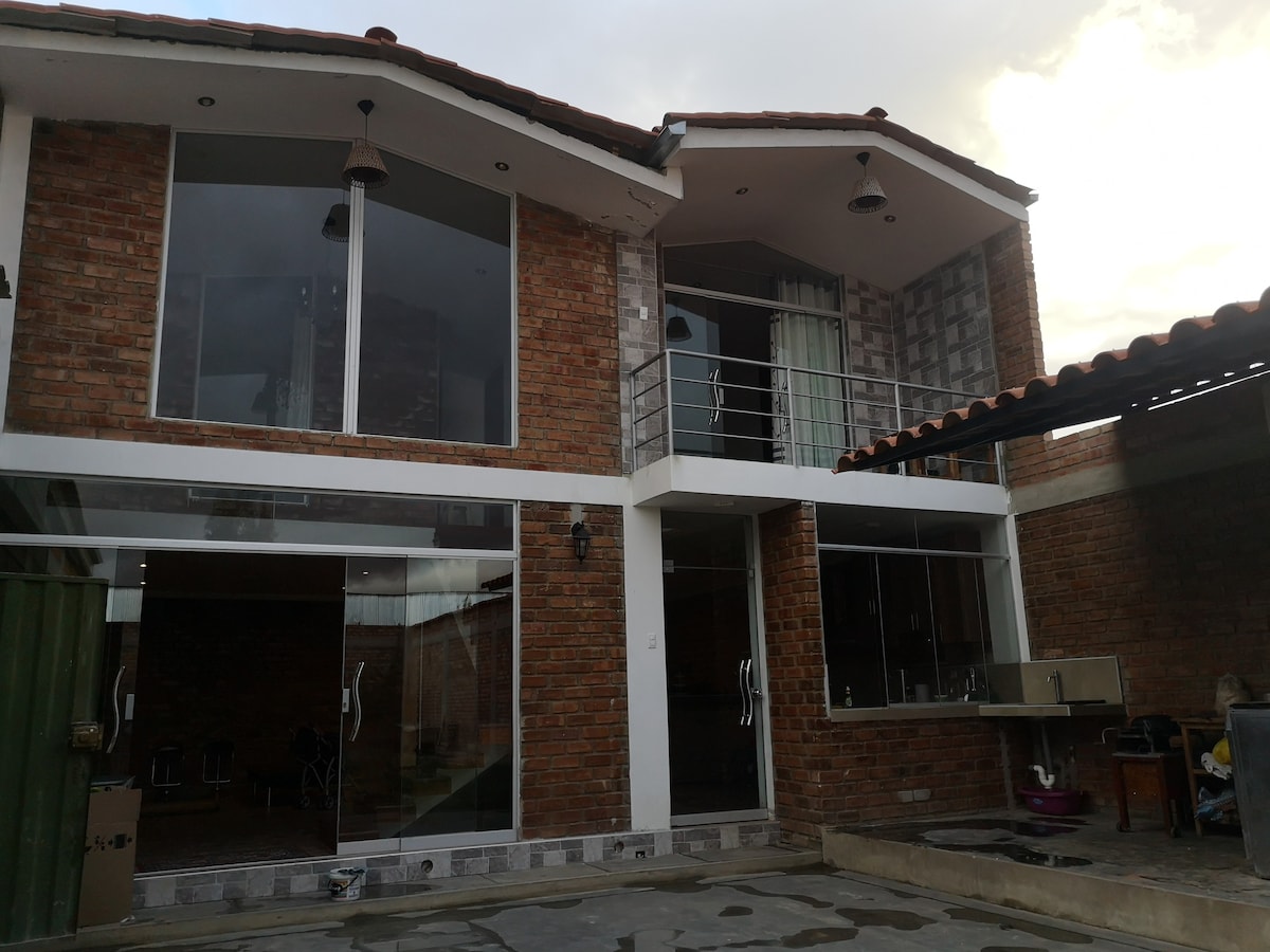 The exterior of the rustic house showcases a modern architectural design, featuring large glass doors that allow for abundant natural light. The brick façade provides a warm contrast to the sleek lines and open spaces. A small balcony is visible on the upper level.
