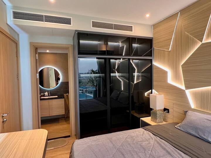 Dormitorio principal con baño en el interior y una gran cama tamaño king, resaltada por la decoración de la pared de madera en muchas conchas marinas. 