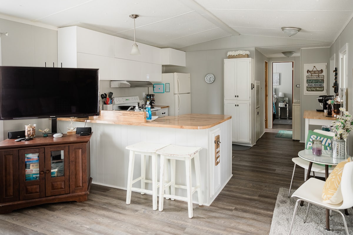 The updated kitchen features modern cabinetry and new appliances. A wooden island with stools provides additional seating. Soft natural light fills the space, highlighting the open layout that connects to the living area and hallway.