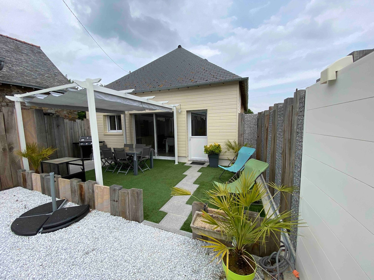 A private outdoor area is visible, featuring a covered terrace and a green lawn. A seating arrangement with chairs and a small table can be seen, along with a barbecue grill. Decorative plants add a touch of greenery to the space, while a lounge chair lies nearby.