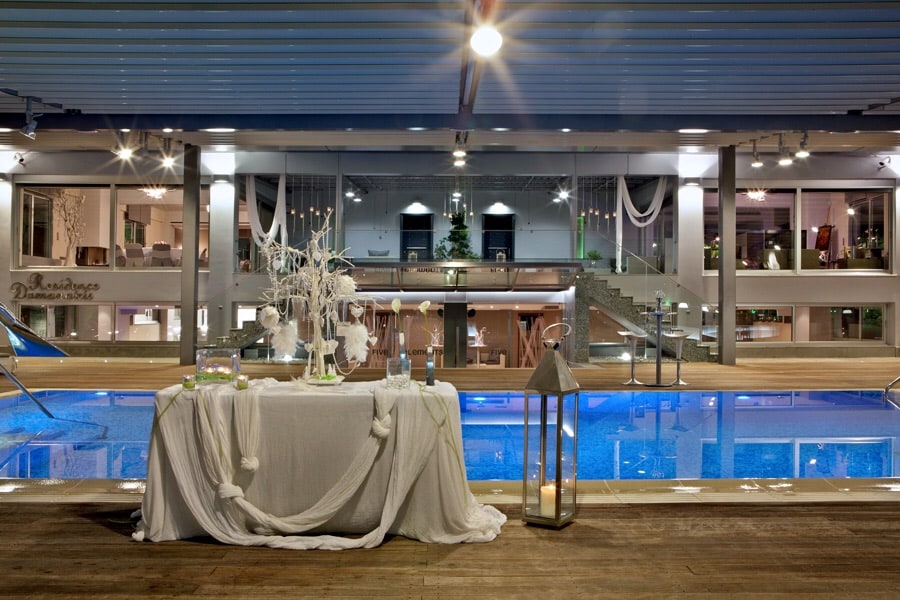 An inviting pool area is highlighted, reflecting soft lights from the surrounding space. A table draped with fabric stands nearby, accompanied by decorative elements. The setting flows seamlessly into an open area with modern furnishings, suggesting an atmosphere suitable for relaxation and gathering.