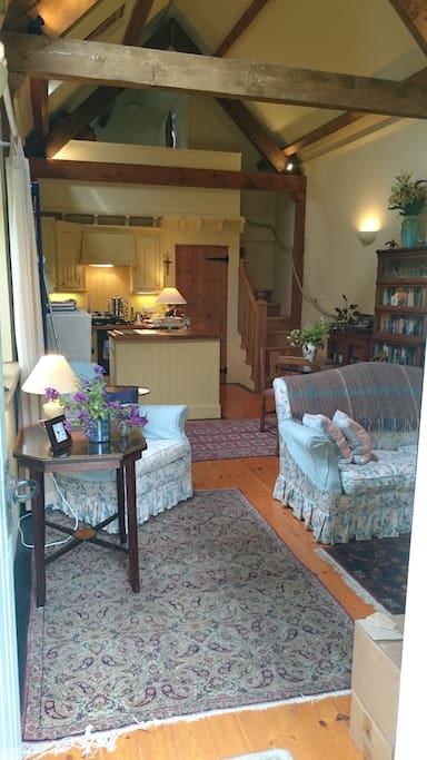 The open plan living area with winding wooden stairs to sleeping gallery and door to single room and shower room.