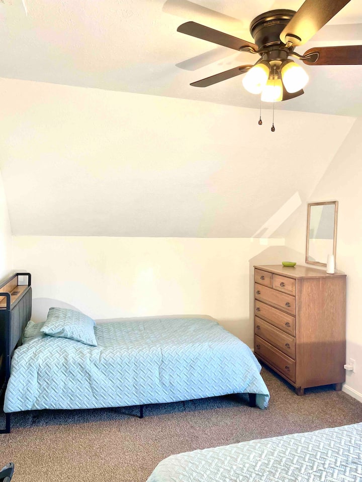 El dormitorio de arriba con una cama tamaño queen y una cama individual también tiene un tocador, un portaequipajes y puertos USB incorporados en los cabeceros.