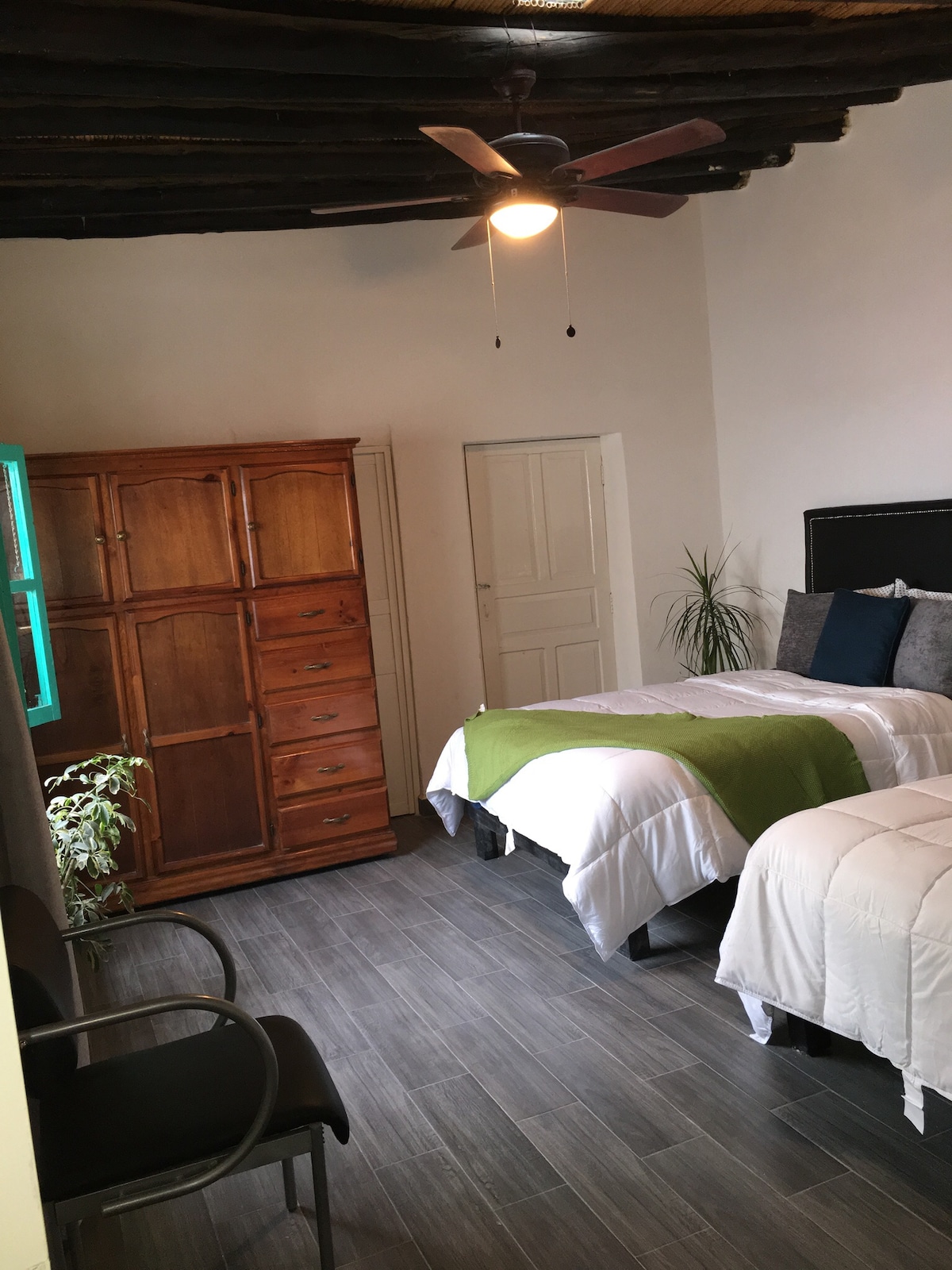 חדר שינה גדול עם שתי מיטות זוגיות, שולחן כתיבה, ארון, כיסא כיסא ומאוורר תקרה. 