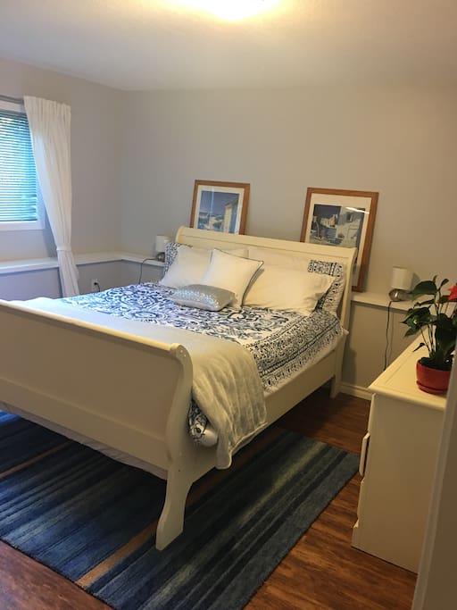 Spacious bedroom with queen size sleigh bed, a small table and a big sunny window.