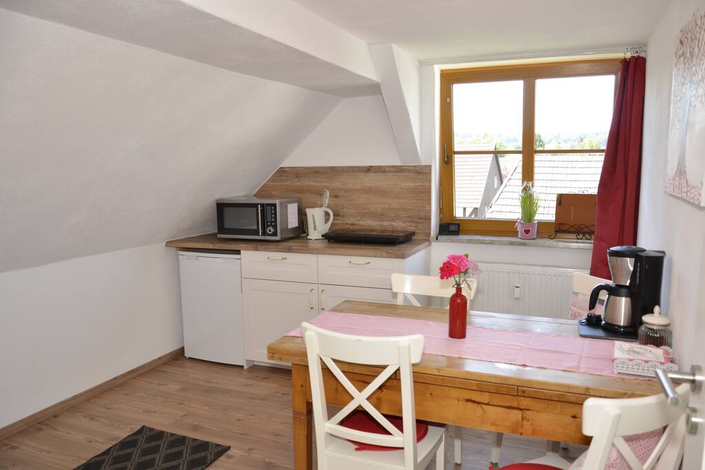 Küche mit Esstisch, Kühlschrank, Mikrowellenofen, Kaffeemaschine und Kochplatten