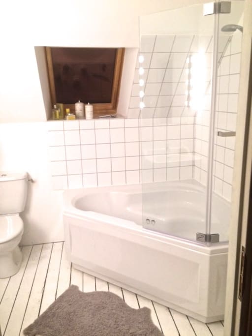Brightly lit all-in-white bathroom with spacious corner bath and shower over