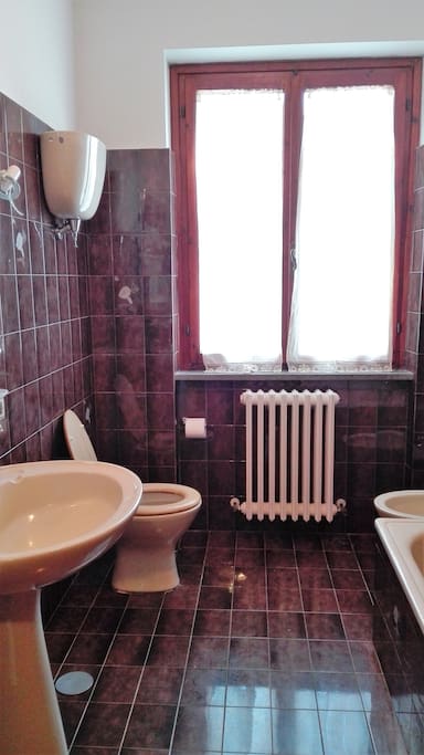 Bagno con vasca sulla destra, lavandino, bidet, termosifone e ampia finestra. Anche se non si vede dalla foto, sopra al lavandino c'è anche uno specchio.