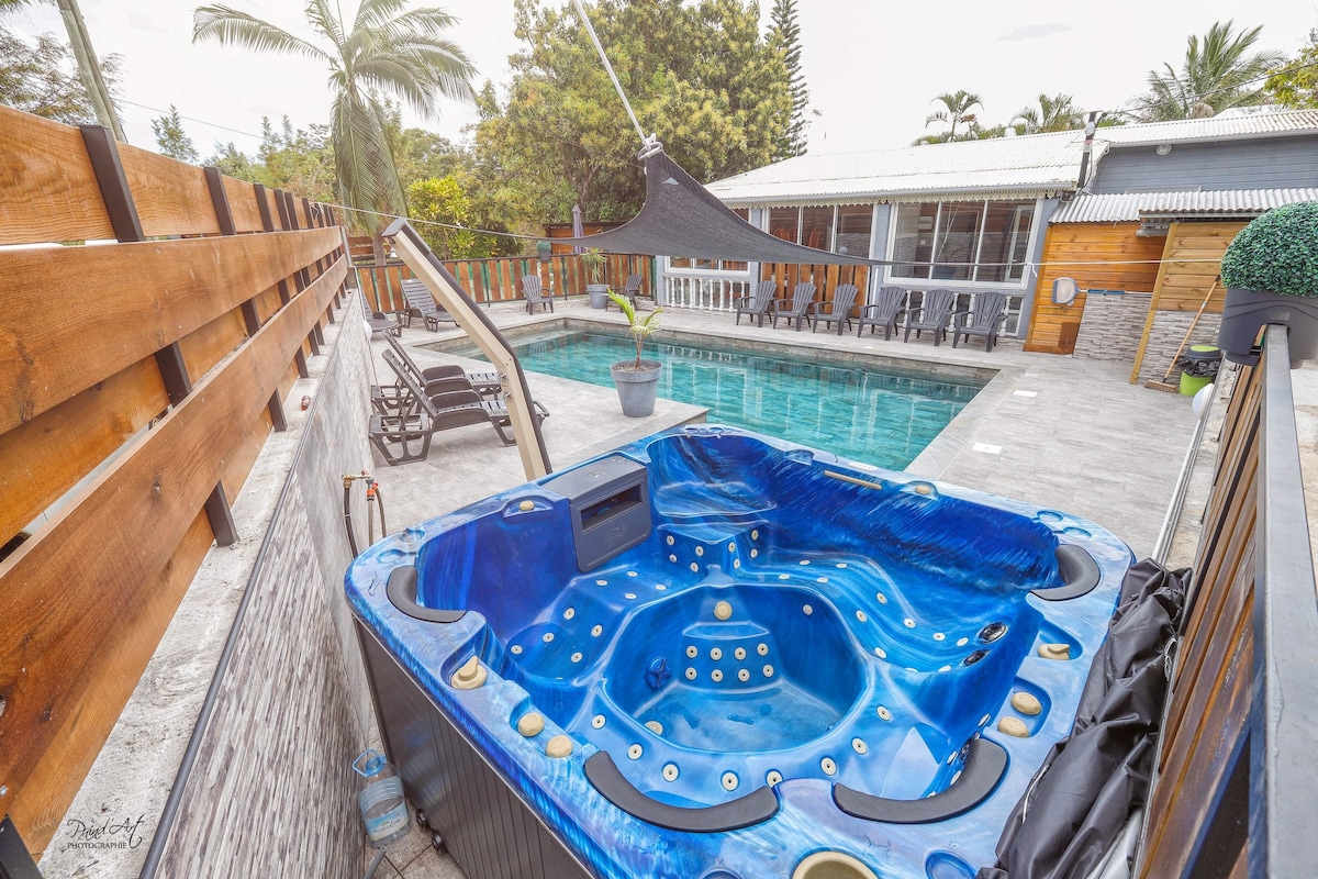 A spacious outdoor area features a bright blue jacuzzi positioned near a large salt-water pool. Surrounding spaces include lounge chairs set against a backdrop of greenery and a shaded seating area, inviting relaxation and comfort.