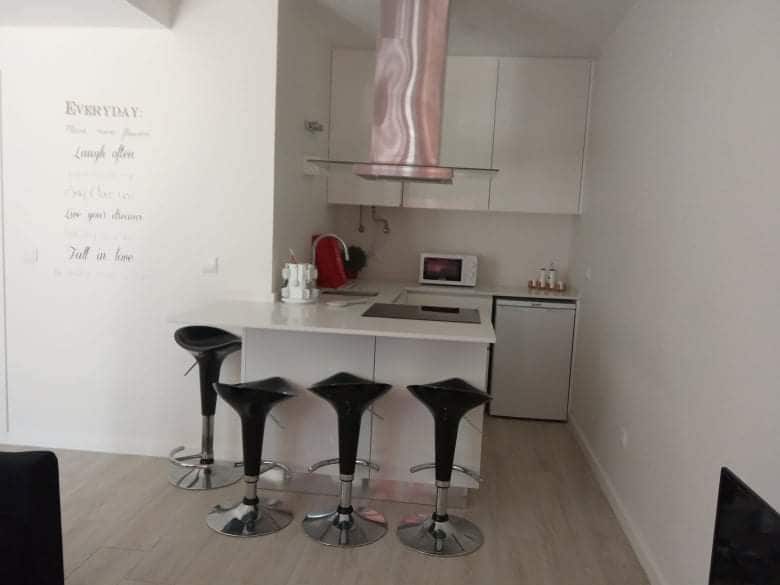 A well-equipped kitchen features modern appliances and a sleek design. Four black bar stools are arranged around a white countertop, creating a space for casual dining or conversation. A stainless steel hood is positioned above the cooking area, contributing to the contemporary aesthetic.
