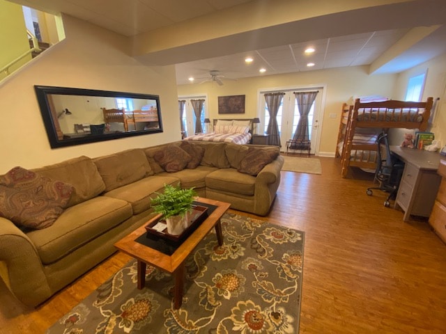 A spacious living area features a comfortable sectional sofa and a coffee table placed on a decorative rug. A work desk is situated beside a set of bunk beds, with ample natural light coming through large windows framed with light curtains.