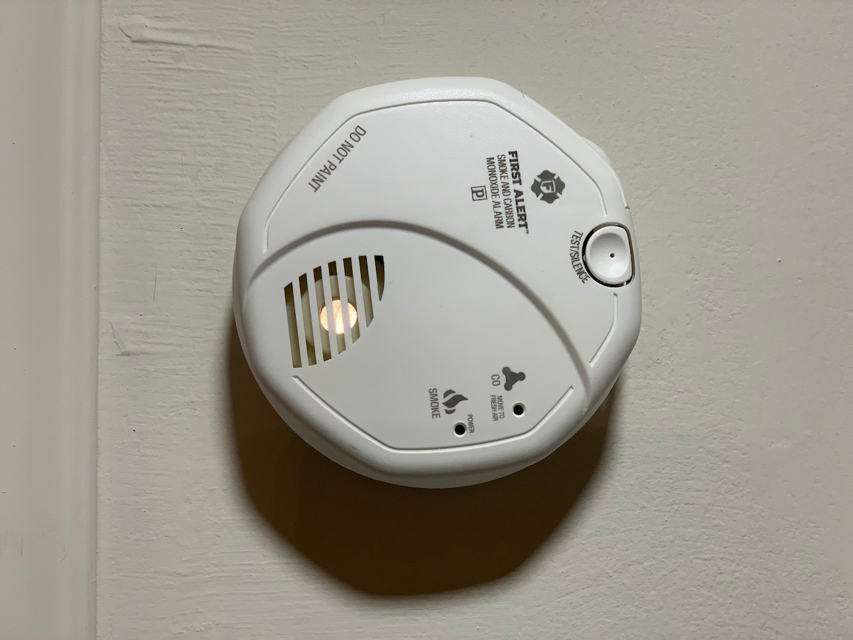 A smoke detector is mounted on the ceiling, featuring a small light that is illuminated. The device includes symbols indicating its functions and safety features, ensuring a secure environment within the suite.