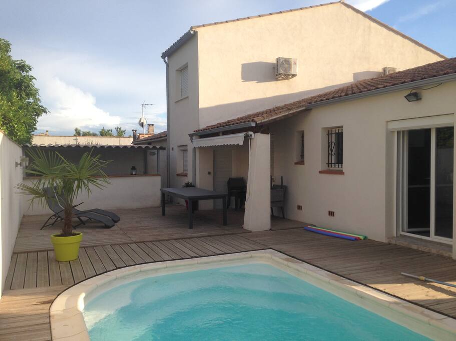 Vue depuis l'angle de la piscine sur la maison et la cuisine d'été au fond