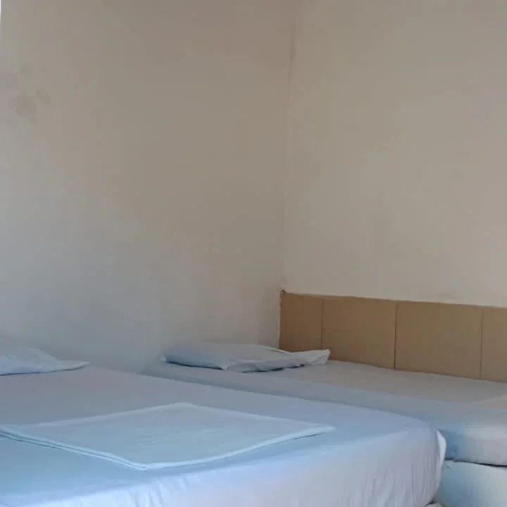 A bright sleeping area is shown, featuring two spacious beds with neutral-colored bedding and several pillows. The light-colored walls enhance the feeling of openness, while soft natural light enters from an unseen window.