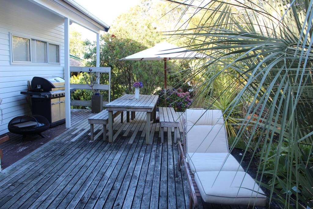 Outdoor entertaining area nestled in amongst a sub-tropical back drop. With BBQ, brazier, outdoor seating and umbrella.