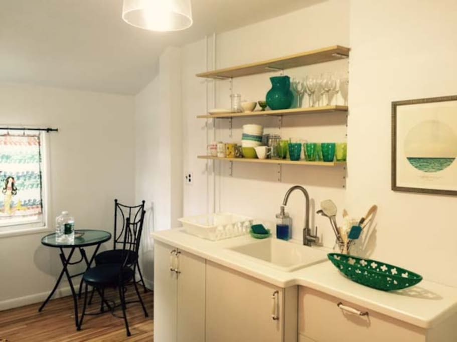 The kitchen contains a fridge, stove, toaster, plates, silverware and pots. a corner nook has a bistro table and 2 chairs , perfect for morning coffee.