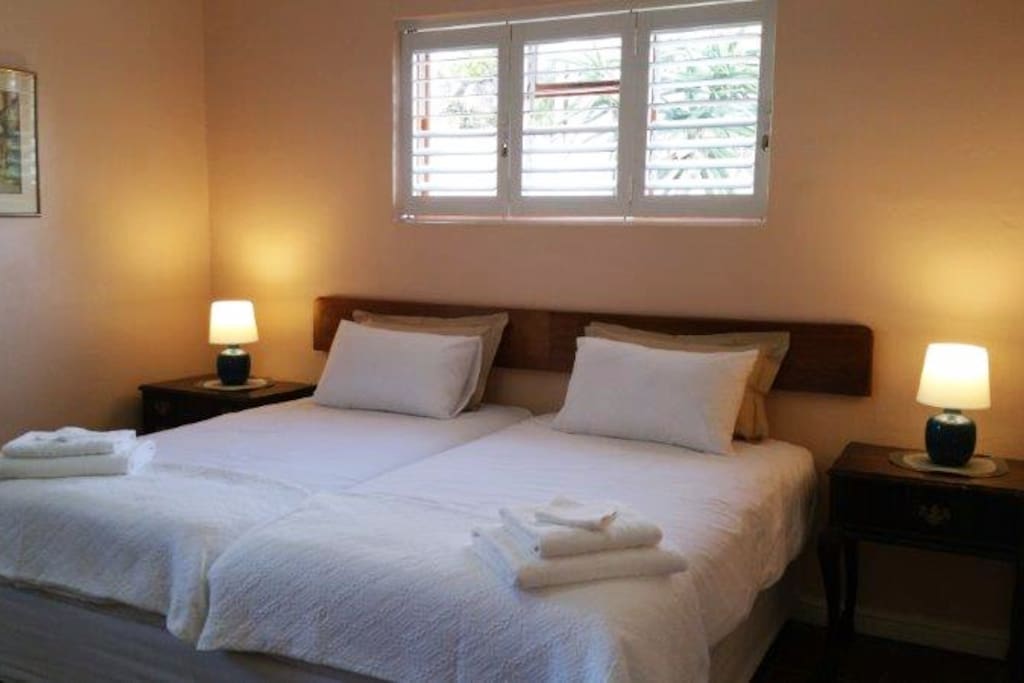 The main bedroom has two 3/4 beds. The wooden windows are secured with aluminium shutters on a steel frame that adjust to allow light to enter the room. Outside is the driveway.