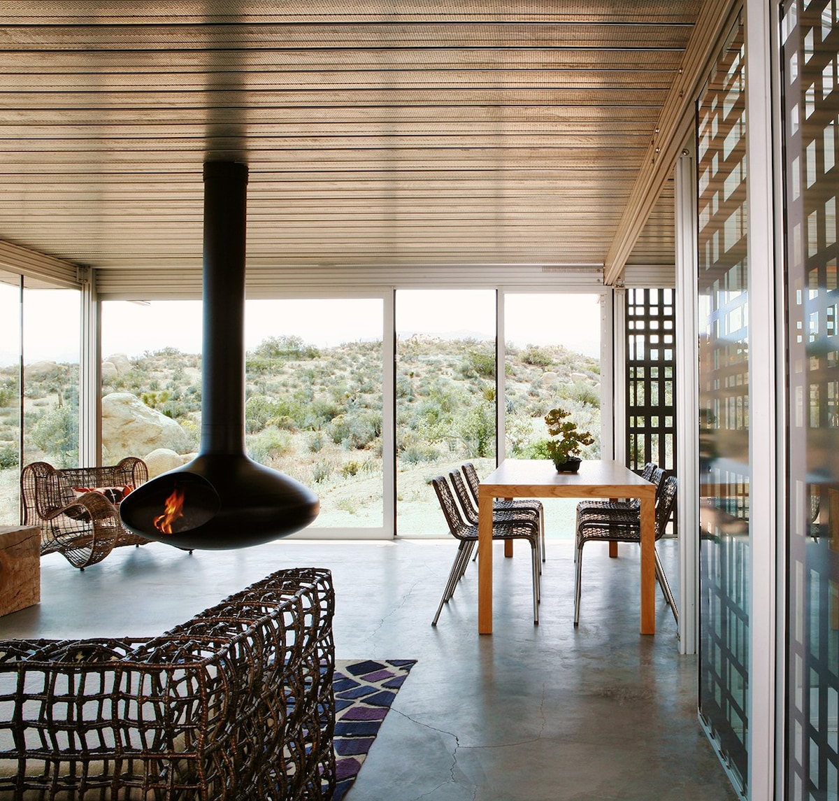 The interior of a Taalman architecture home shows a wooden ceiling, stone floors and a fireplace that’s suspended by its chimney.