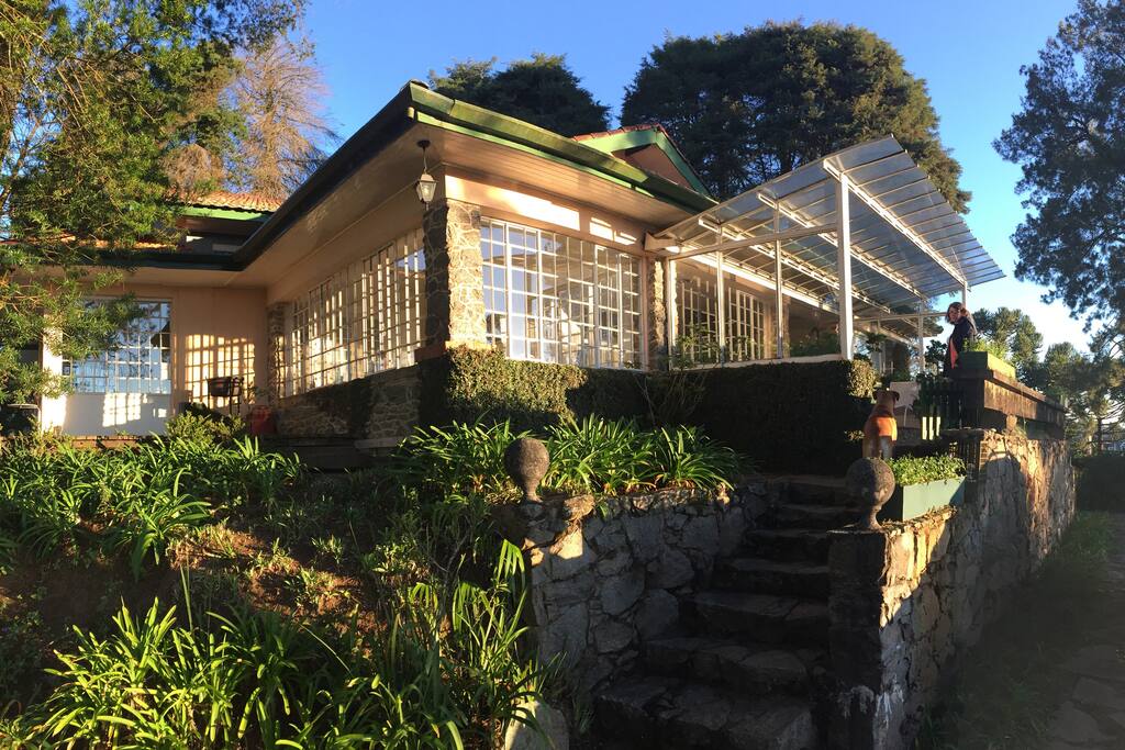 A casa, com fachada de pedras naturais e vidro, ao por do sol.