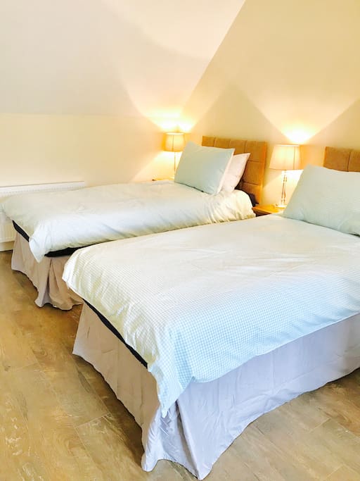 One half of large bedroom with two single beds. Each bed has its own bedside table. Lots of surface space and seating out of view.