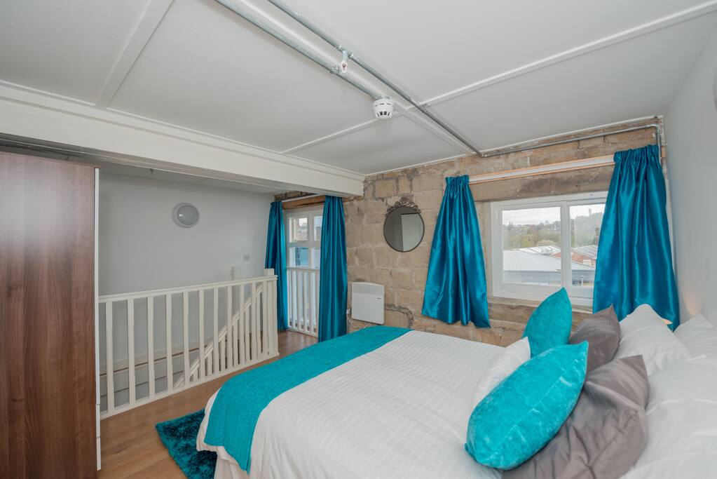 Bedroom on a mezzanine floor, with wardrobe, two chests of draws, chairs, bedside lamps, two mirrors and a hairdryer.
