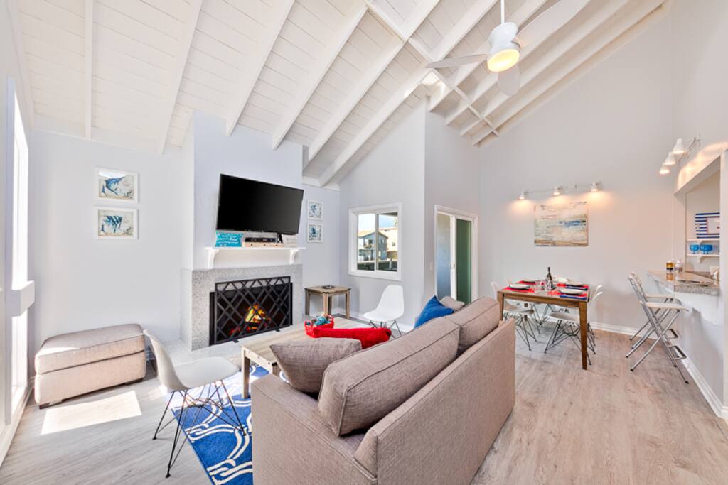 Clean, beach chic great room with a large flat screen TV, a fireplace, comfortable seating, and ceiling fan.