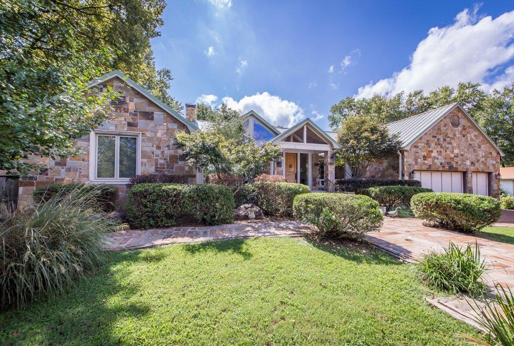 The exterior of the Chateau showcases a blend of stone and wood elements, framed by well-maintained landscaping. A welcoming pathway leads to the entrance, which is flanked by lush greenery and features a charming gabled roof under a bright blue sky.