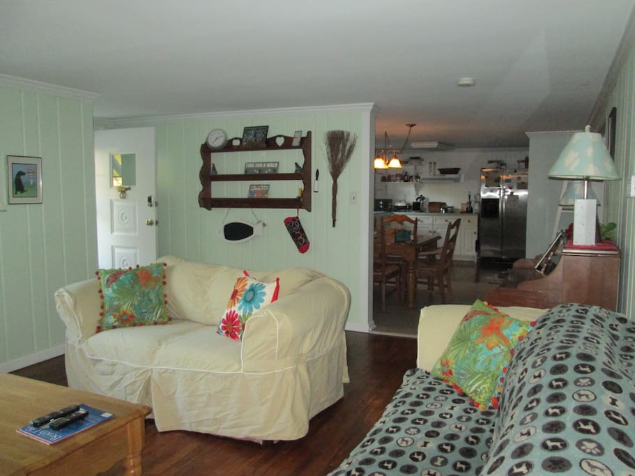 View from living room to kitchen. Living room has queen sofa bed, love seat , piano and TV.