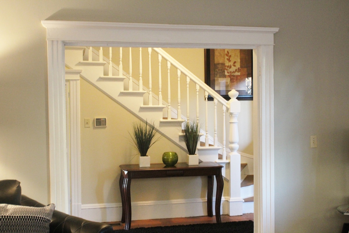 A traditional staircase showcases elegant white banisters leading to the upper levels of the home. A small console table adorned with simple greenery is positioned beneath the stairway, adding a touch of tranquility to the entryway.