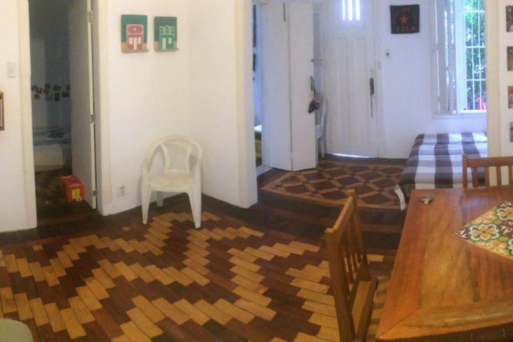 Sala de uso comum, com wifi, mesa de jantar, sofá-cama de casal e ventilador. Iluminada e arejada, com janelas amplas que dão para quintal externo e portas para ambos os quartos, corredor e cozinha.