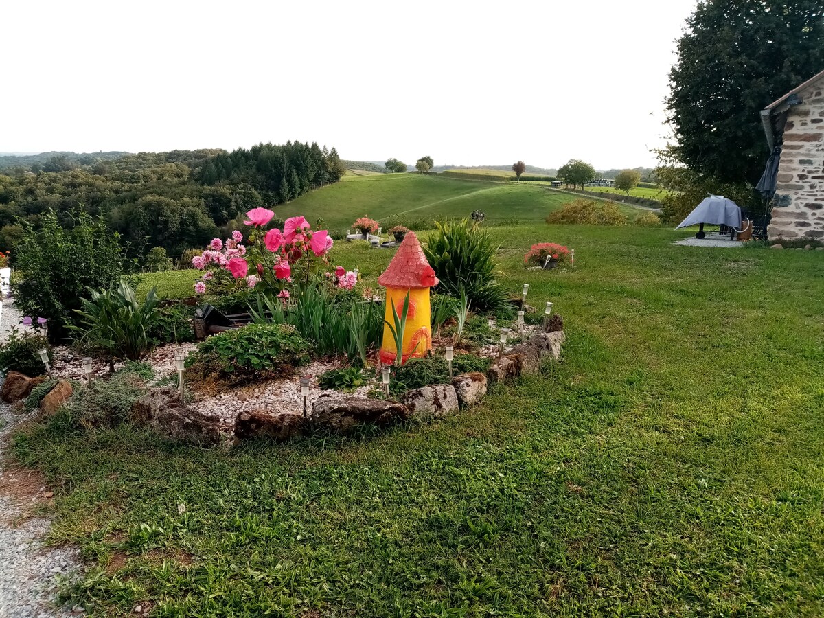 A well-maintained garden is highlighted by colorful flowers, including pink peonies, surrounding a whimsical mushroom statue. The lush green lawn seamlessly blends with the rolling hills in the background, creating a serene outdoor space that invites relaxation.