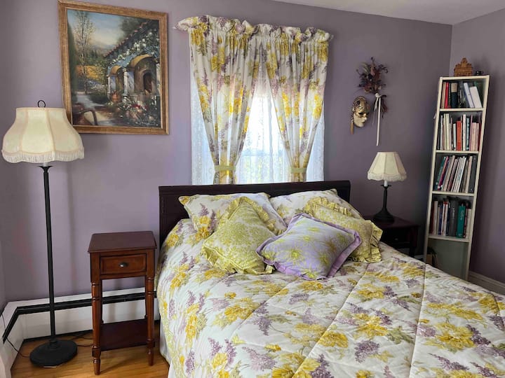 تحتوي غرفة أرجواني على سرير كامل وستائر لتقليل أشعة الشمس في الصباح.