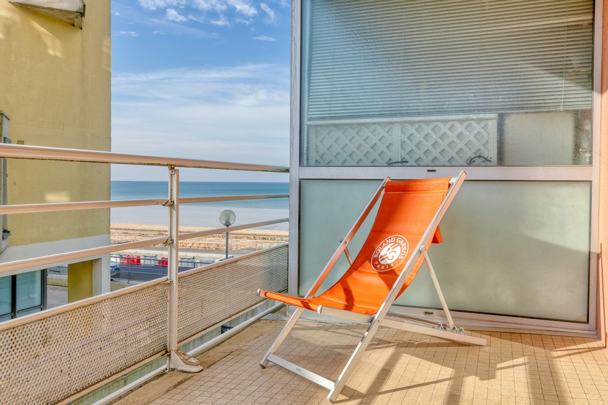 A bright terrace with an orange lounge chair faces the sea. The expansive ocean view is visible beyond the railing. The surrounding area features a light-colored tiled floor, contributing to a serene outdoor space for relaxation.