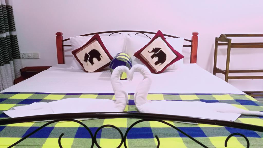 A spacious bed draped in white linens, featuring decorative pillows with elephant motifs. The bedding is complemented by a colorful checkered throw at the foot of the bed. A towel arrangement resembling a heart shape is placed on the bed, adding a charming touch to the setting.