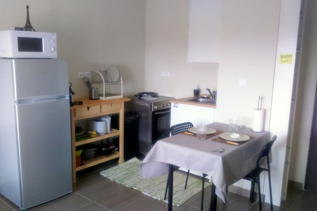 Cuisine avec tout le nécessaire pour cuisiner (assiettes, verres, couverts, poêle, casserole, machine à café, bouilloire, grille pain, four, plaques vitro-céramique, frigo, congélateur, ...)