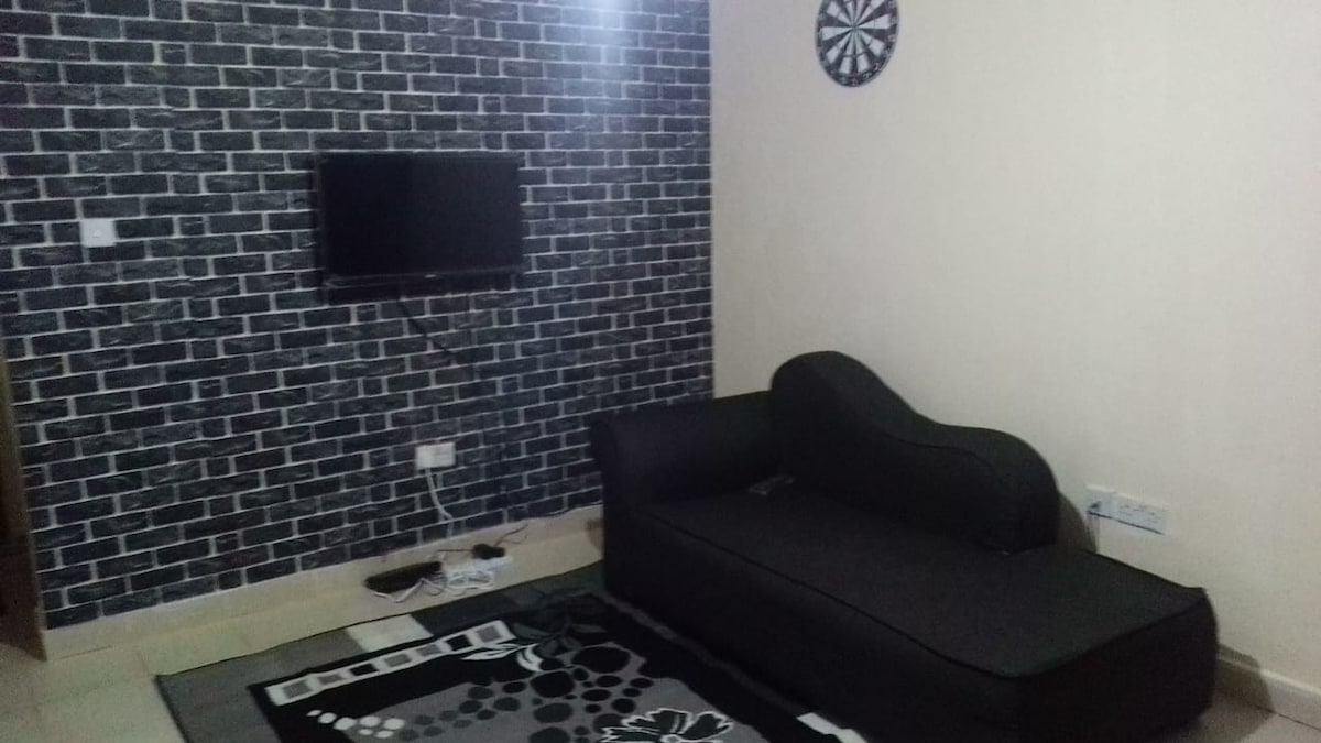 A cozy living area is presented with a black and white brick wall design. A contemporary black couch is positioned facing a mounted television. A patterned rug covers the floor, contributing to the inviting atmosphere of the space.