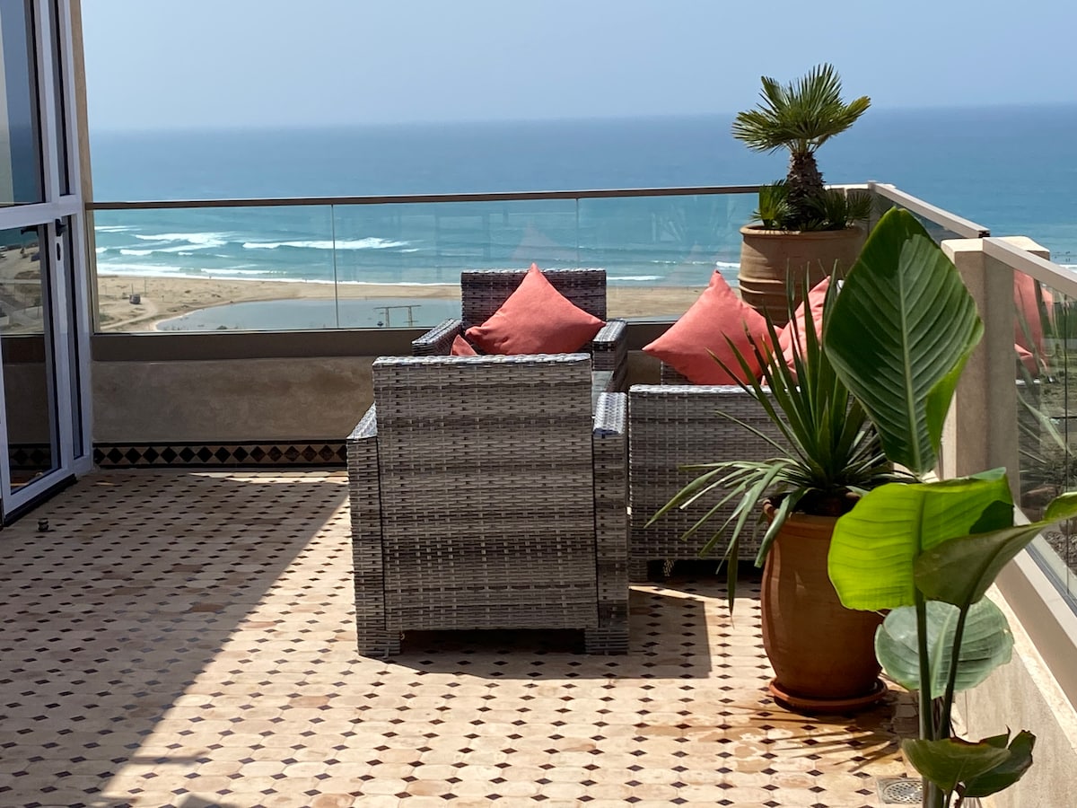 A spacious terrace offers panoramic views of the ocean, featuring comfortable seating with cushions and decorative potted plants. The area showcases tiled flooring, enhancing the relaxation space for guests.