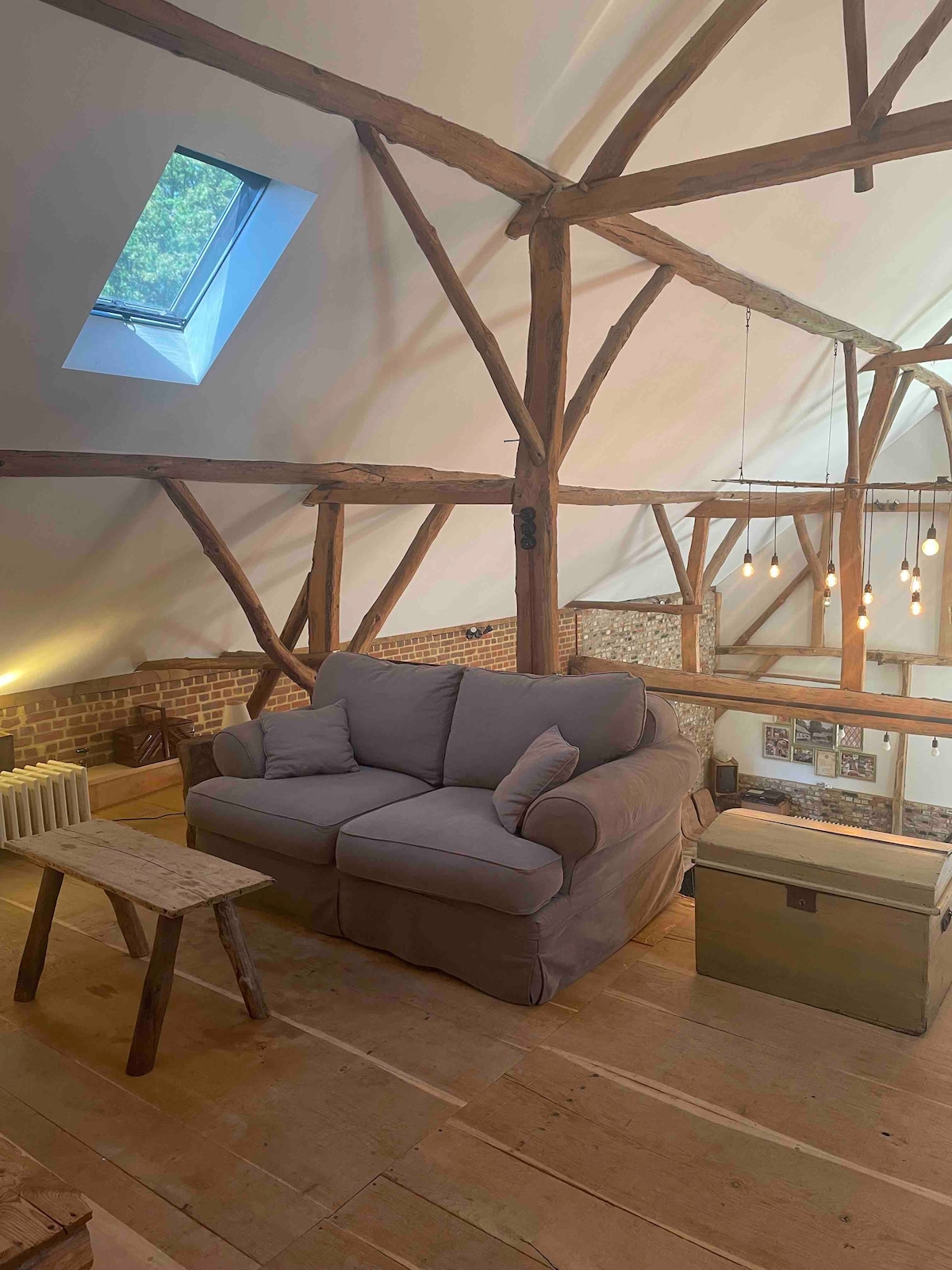 A cozy seating area features a plush, light-colored couch positioned next to a rustic wooden table. Exposed wooden beams add architectural interest to the high ceiling, and a skylight allows natural light to illuminate the space.