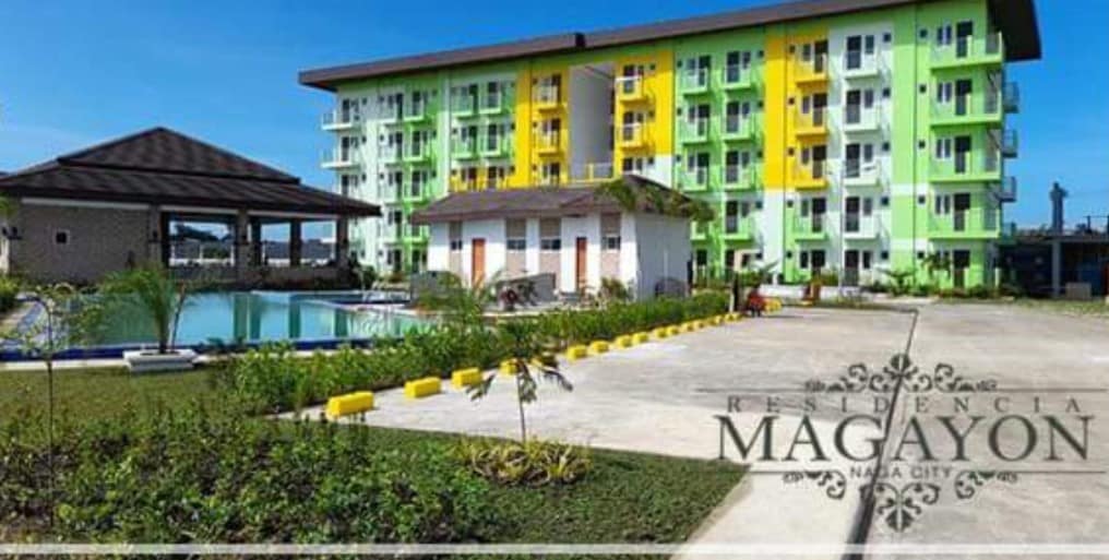 The exterior view showcases a multi-story condominium building featuring a modern design with vibrant green and yellow accents. A swimming pool is visible in the foreground, surrounded by neatly trimmed grass and decorative landscaping. Ample parking space is also presented.