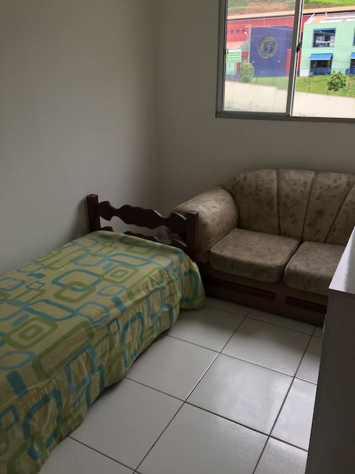 Quarto solteiro com cama , sofá, e cômoda com gavetas e espaço.