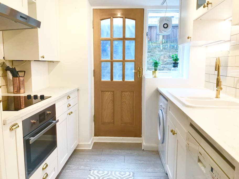 Brand new trendy kitchen features marble worktops, grey wood flooring and fresh white cabinets with brass fittings with the door opening into the garden
