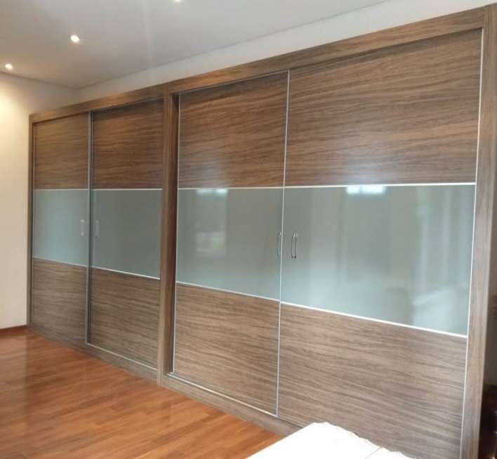 A modern wardrobe is displayed, featuring sliding doors with a combination of wood and frosted glass panels. The warm wooden tones complement the hardwood flooring, contributing to a clean and organized appearance in the room.