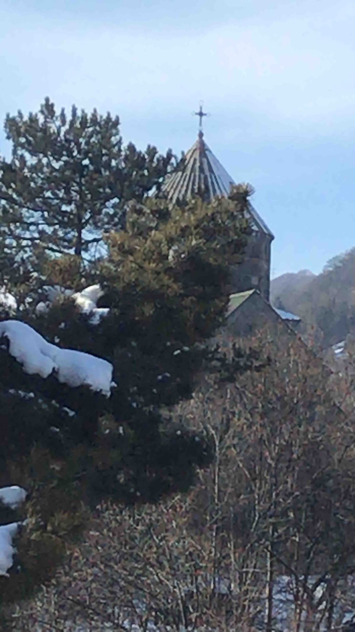 A snow-covered area features a church with a distinct spire in the background, surrounded by trees. The scene captures an atmosphere of tranquility, with soft white snow contrasting against the earthy tones of the landscape.