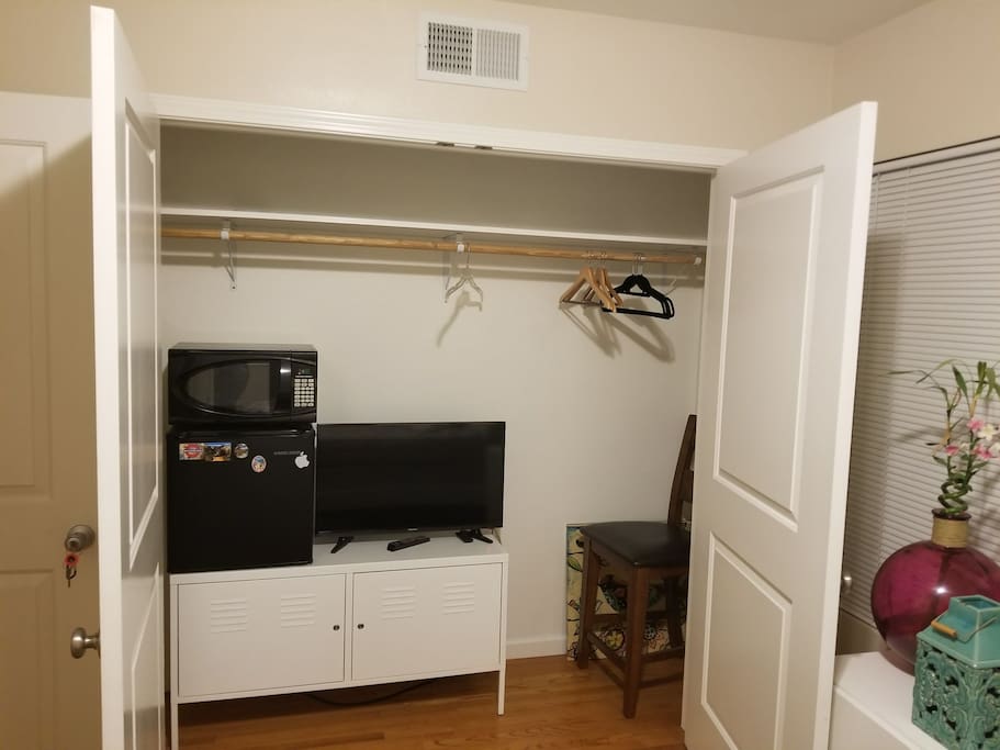Closet with mini fridge, microwave, television, and cabinet with locks for personal items.