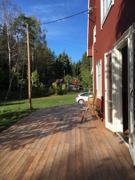 Stor veranda i soligt läge. I bakgrunden skymtas ladan, carporten och det lilla gästhuset.