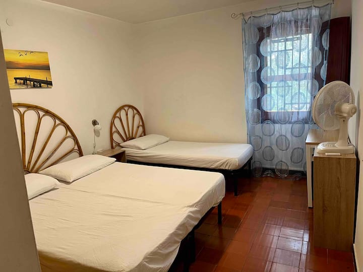 Dormitorio uno con una cama doble separable, una cama individual y un ventilador remoto