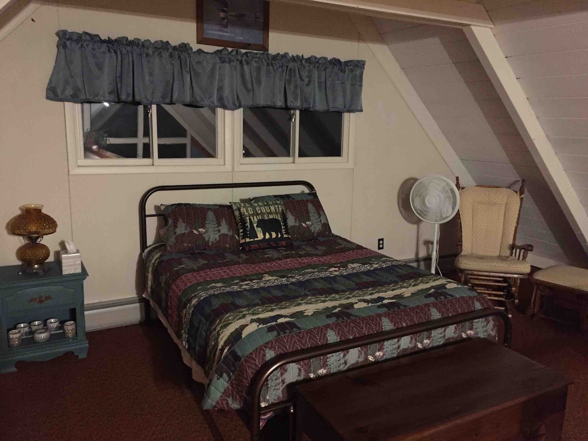 Spálňa s manželskou posteľou, ktorá siaha do podkrovia. Na fotke podkrovia je malá pohovka so starožitným písacím stolom. Určite najlepšia izba s výhľadom. 