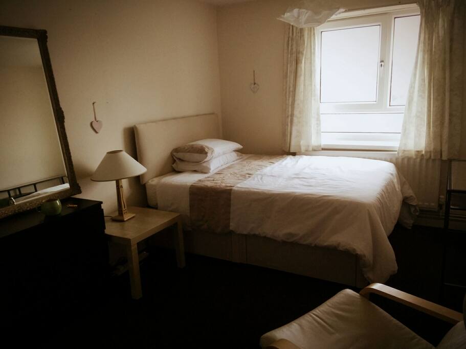Double bedroom with chest of drawers, desk, chair and built in wardrobe.