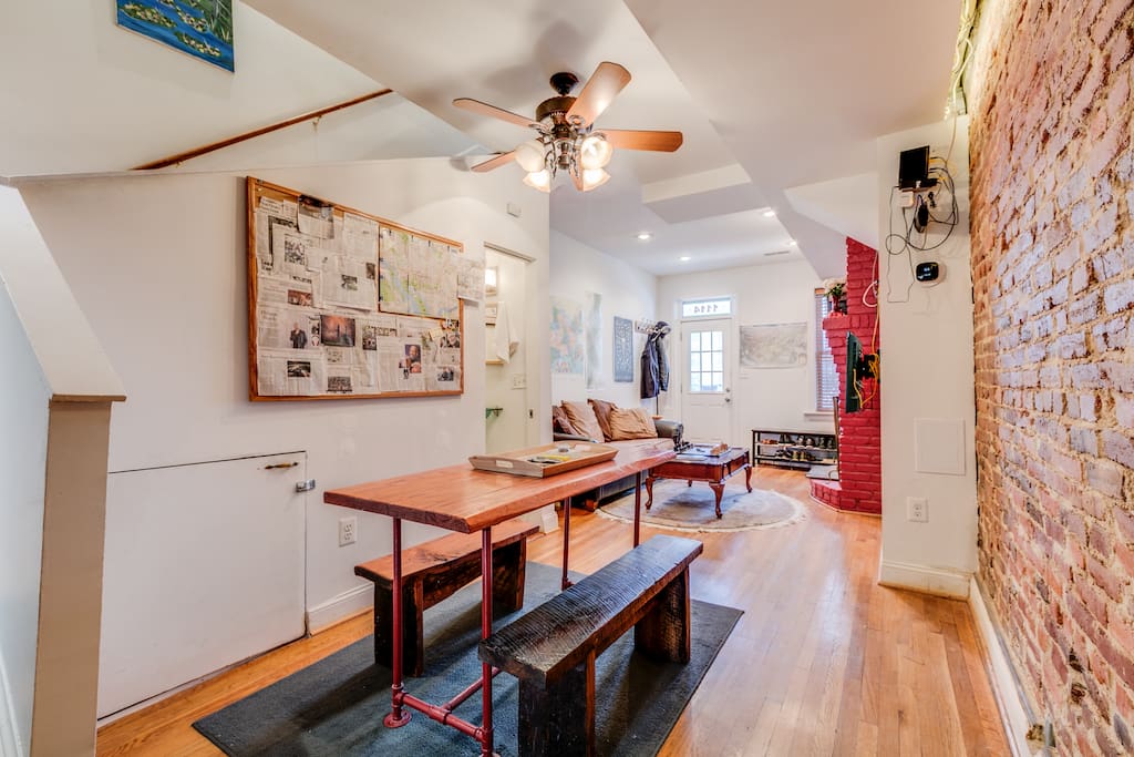 The dining area features a custom-built wood dining table and a cork board displaying not only a map of the District with places of interest for guests to check out, but also a curated rotating collage of recent newspaper articles of interest. The room is framed by an exposed brick wall, stunningly back-lit along the ceiling.